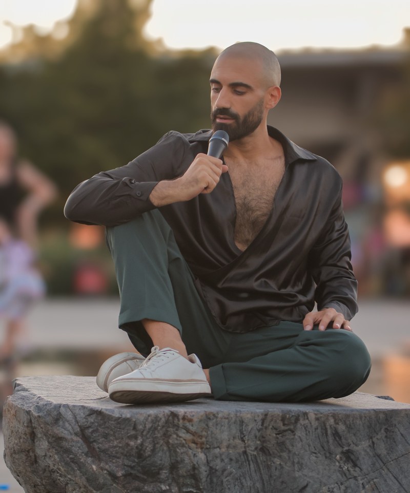 Sami Harb seated outdoors at golden hour, singing into a microphone